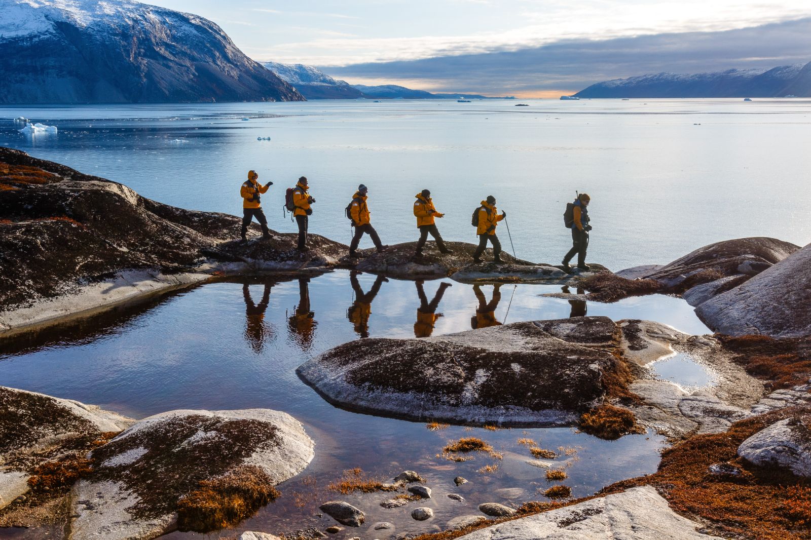 Hikers reflected in still Arctic fjord waters in Greenland
