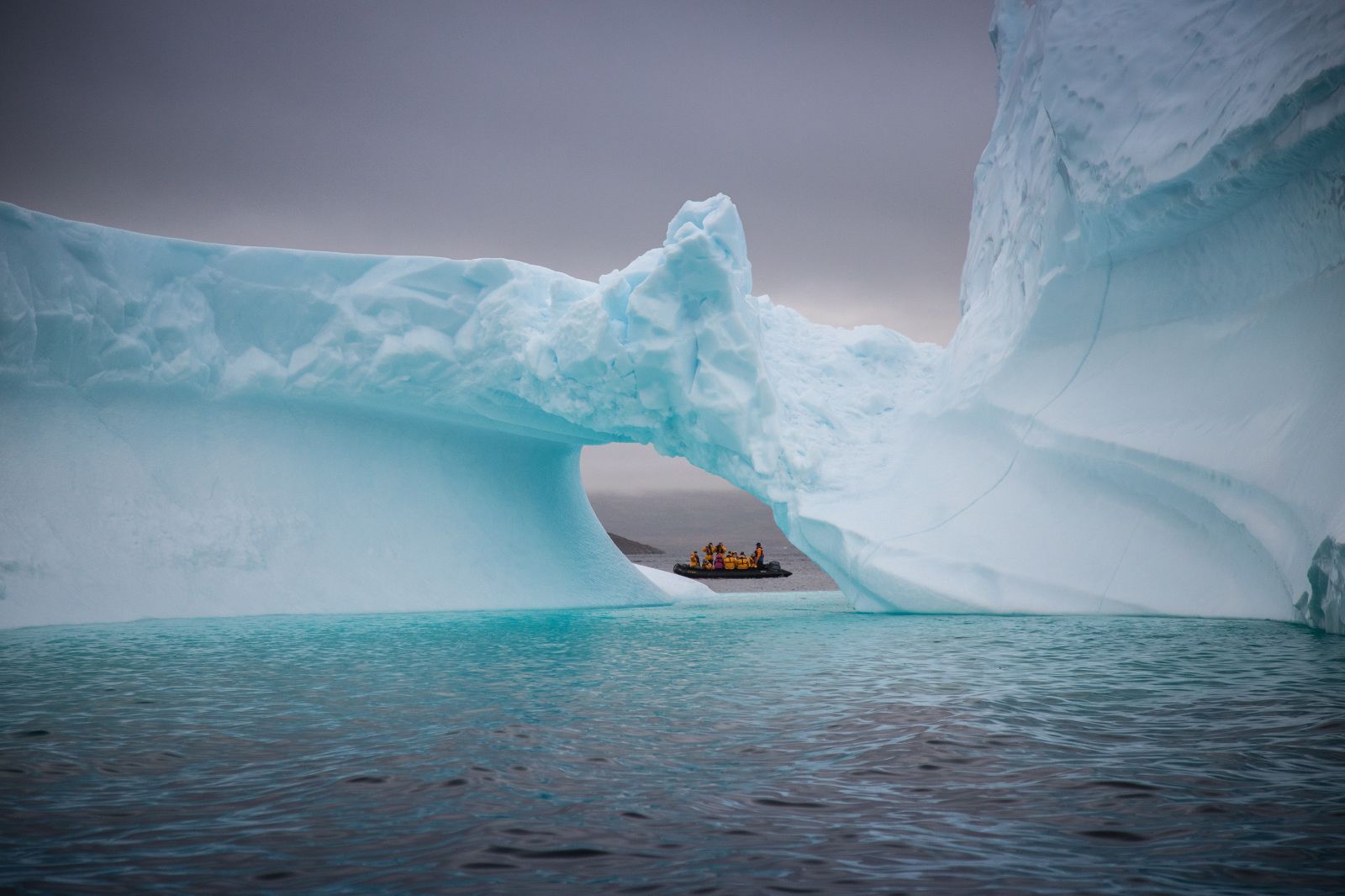 A Zodiac boat seen through the arch of an iceberg in the Arctic