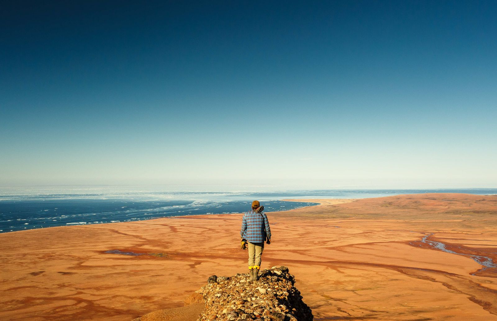 Man on a cliff looking out over Arctic wilderness in Somerset Island, Canada