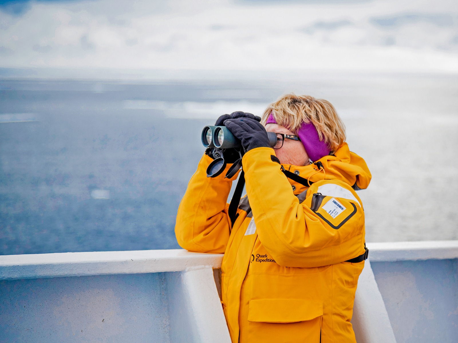 A woman using binoculars onboard Quark Expeditions' Ultramarine in the Arctic