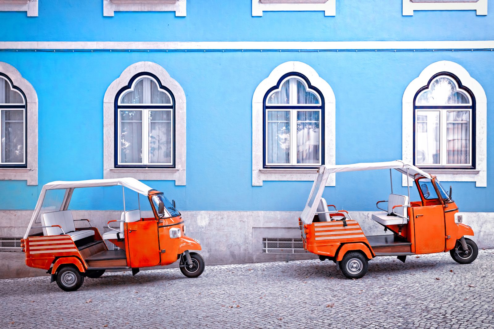 Bright red tuk-tuks parked by a pastel blue building in historic Lisbon
