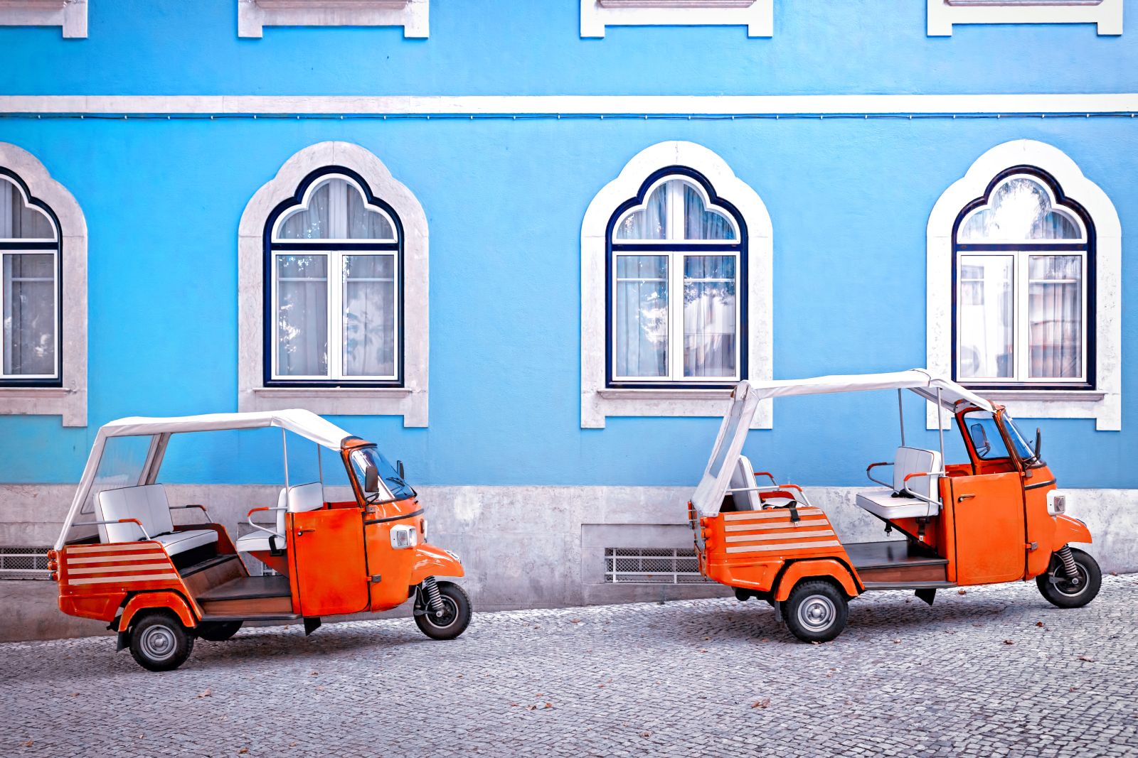 Bright red tuk tuks parked by a pastel blue building in historic Lisbon