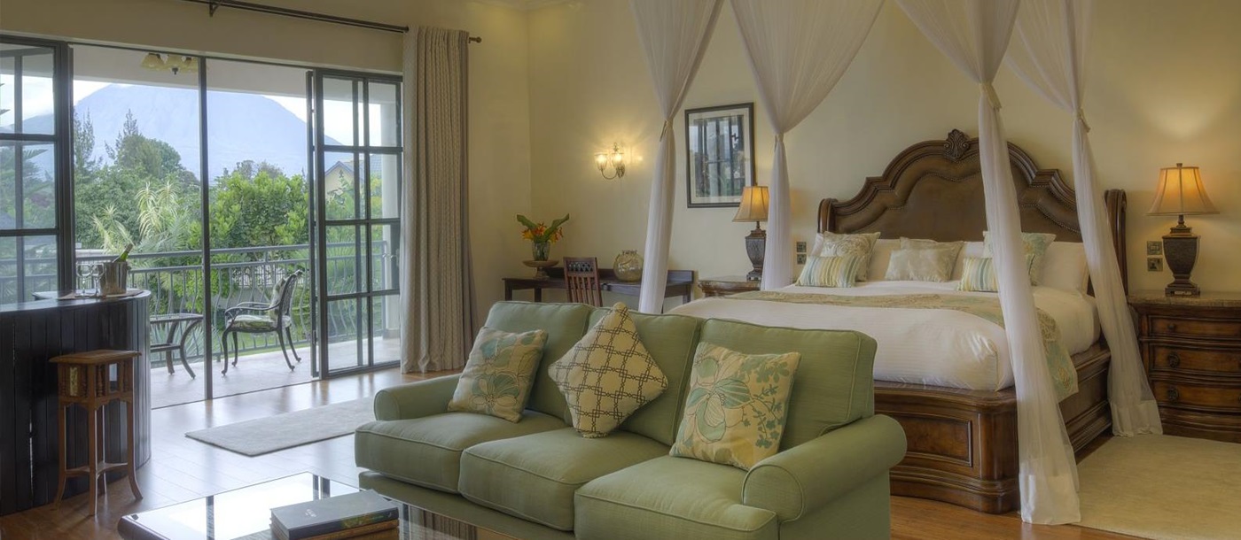 A bedroom suite with double bed, sofa, table, corner bar and outdoor balcony with a table and chairs at The Bishops House hotel in Rwanda 
