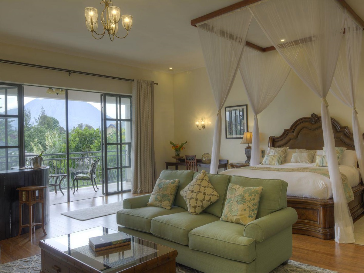 A bedroom suite with double bed, sofa, table, corner bar and outdoor balcony with a table and chairs at The Bishops House hotel in Rwanda