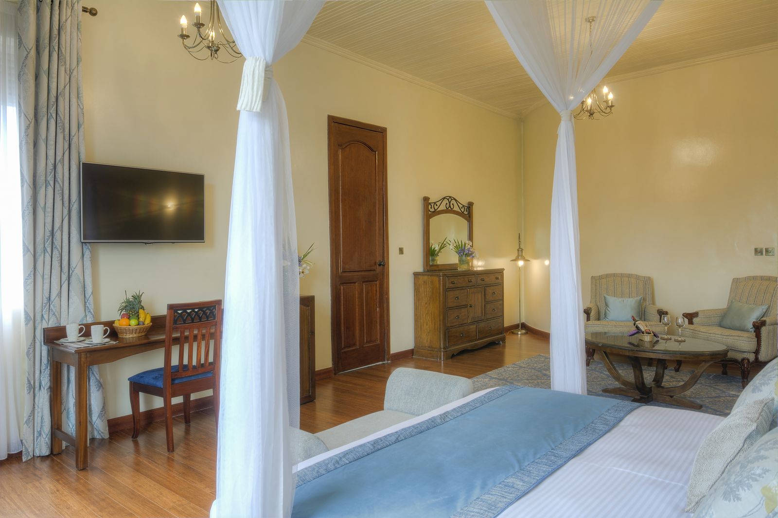 A double bedroom suite at The Bishops House hotel in Rwanda with chairs and a table and a flat screen TV on the wall