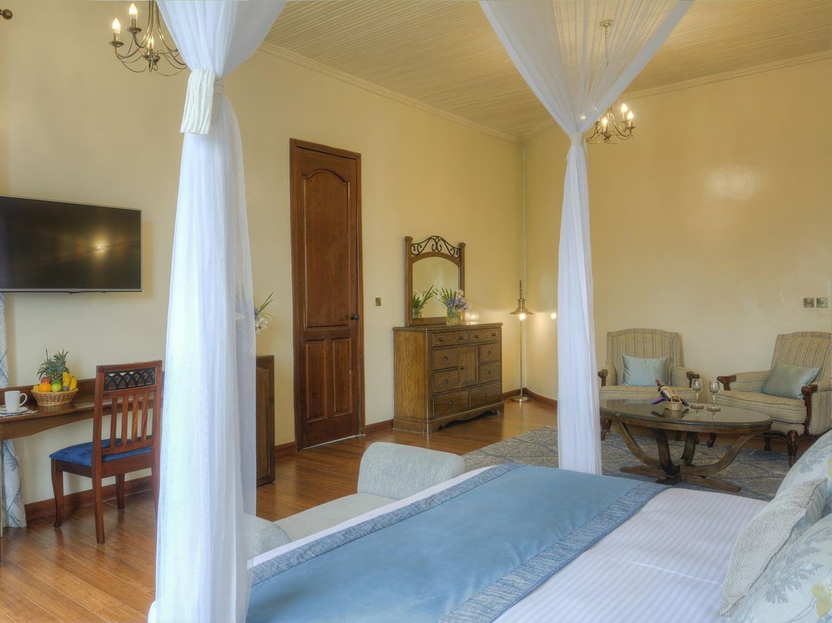 A double bedroom suite at The Bishops House hotel in Rwanda with chairs and a table and a flat screen TV on the wall