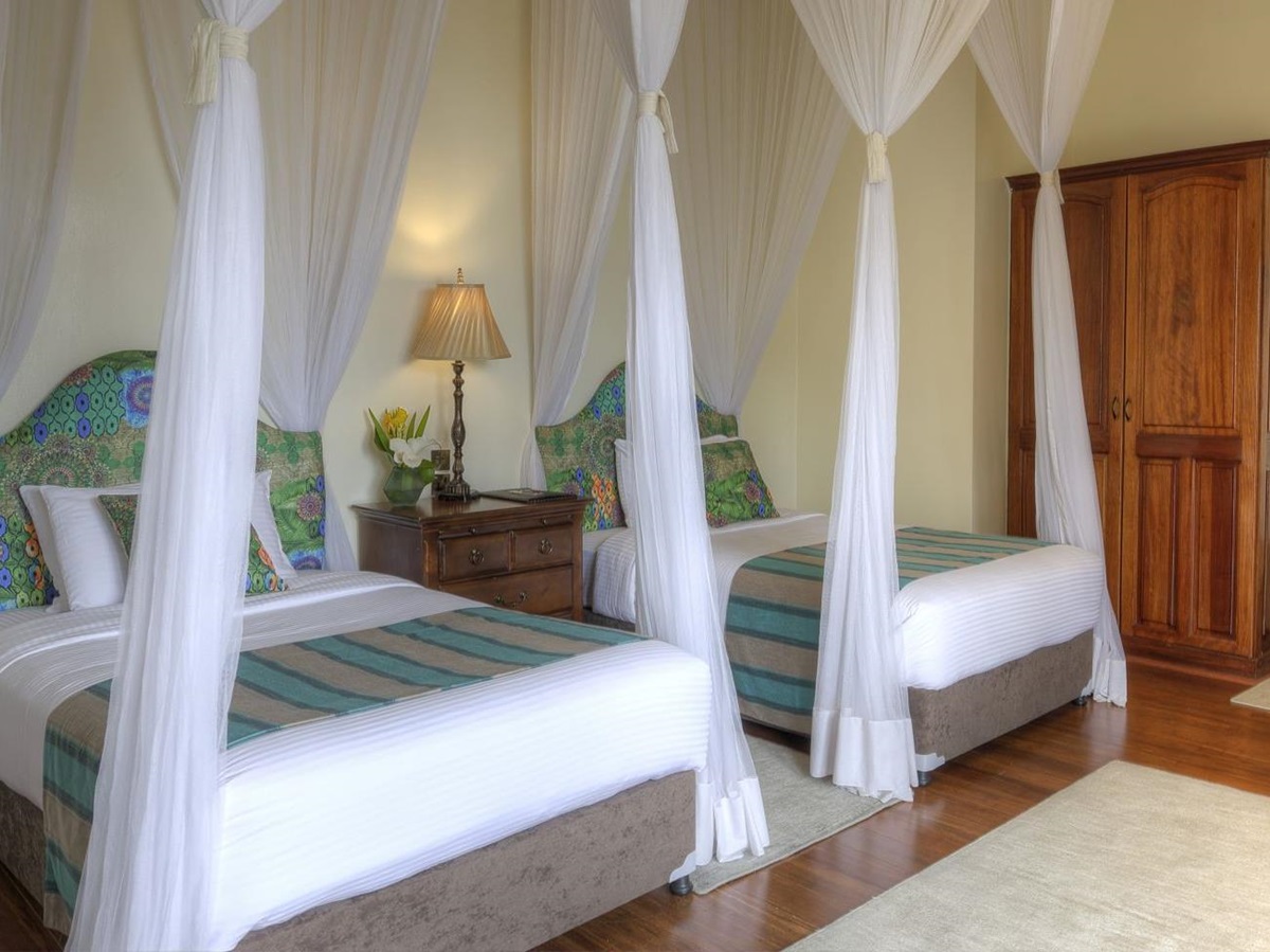 A twin bedroom at The Bishops House hotel in Rwanda with two large single beds a wardrobe and chair