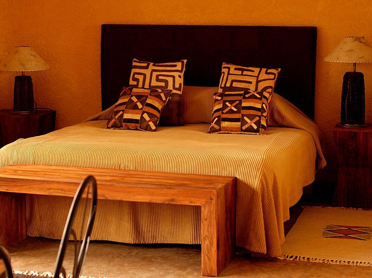 A double bedroom with gold coloured linen and wood furniture at Sabyinyo Silverback Lodge in Rwanda