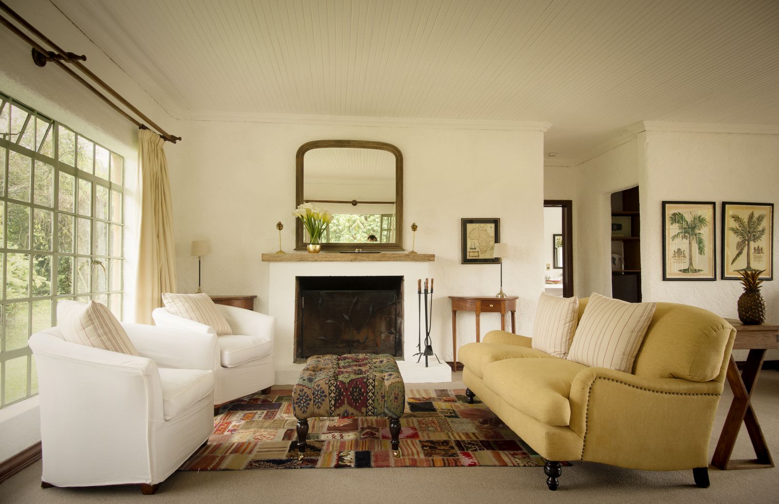 A small sitting room with a yellow sofa and two white chairs in front of a fireplace at Sabyinyo Silverback Lodge in Rwanda
