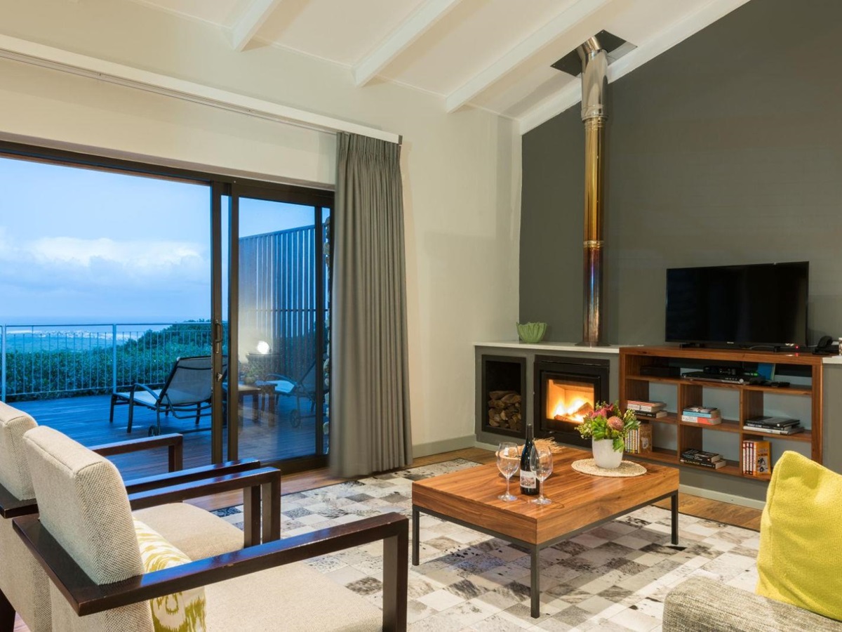 Garden lodge living area with indoor fireplace and sliding doors out onto private terrace at luxury lodge Grootbos Garden Lodge in South Africa