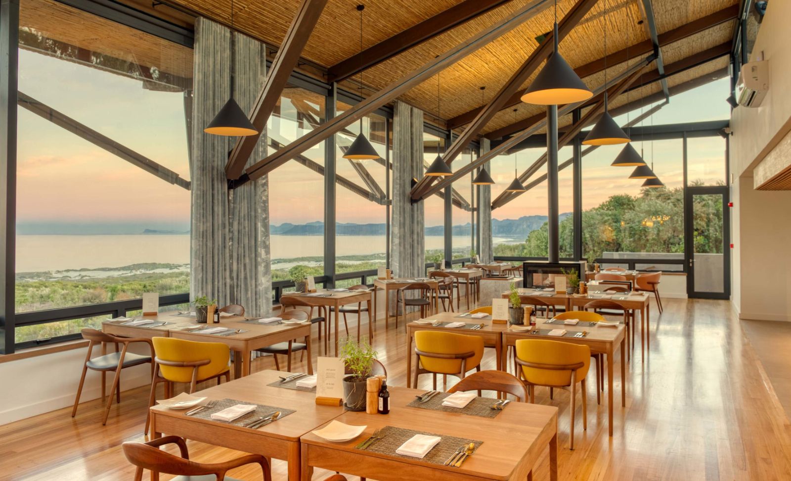 Indoor restaurant with wooden beams and bright floor -to-ceiling windows at luxury lodge Grootbos Garden Lodge in South Africa