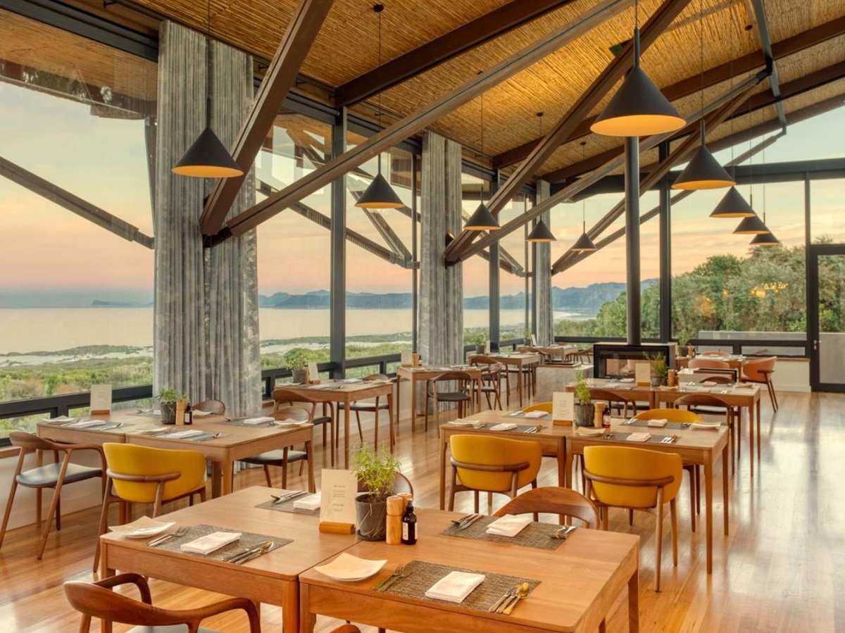 Indoor restaurant with wooden beams and bright floor -to-ceiling windows at luxury lodge Grootbos Garden Lodge in South Africa