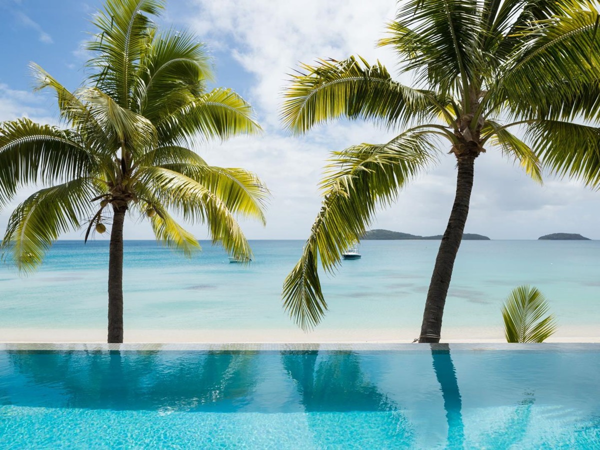 View over a villa pool and the palm-strewn beach to the Pacific Ocean at luxury resort Kokomo Island in Fiji