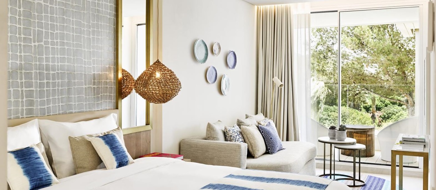 Spacious deluxe room with seating area and private balcony overlooking the gardens at luxury hotel Nobu Ibiza