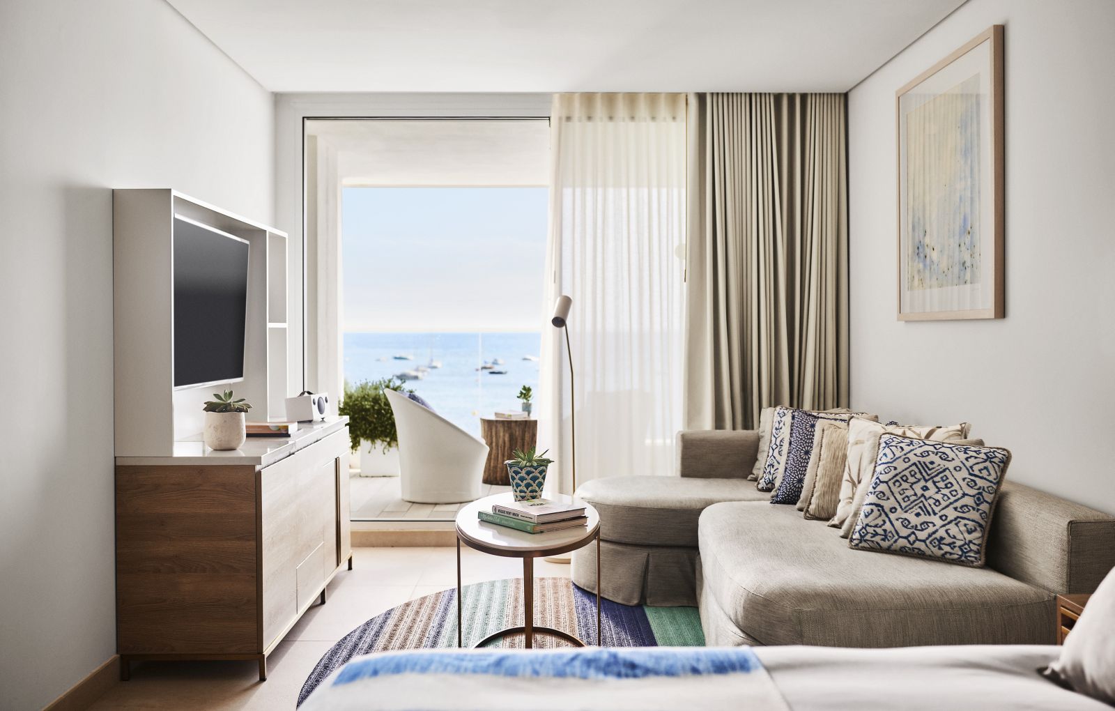 Interior of a Junior Suite with Sea View, private balcony and seating area with flat-screen TV at luxury hotel Nobu Ibiza