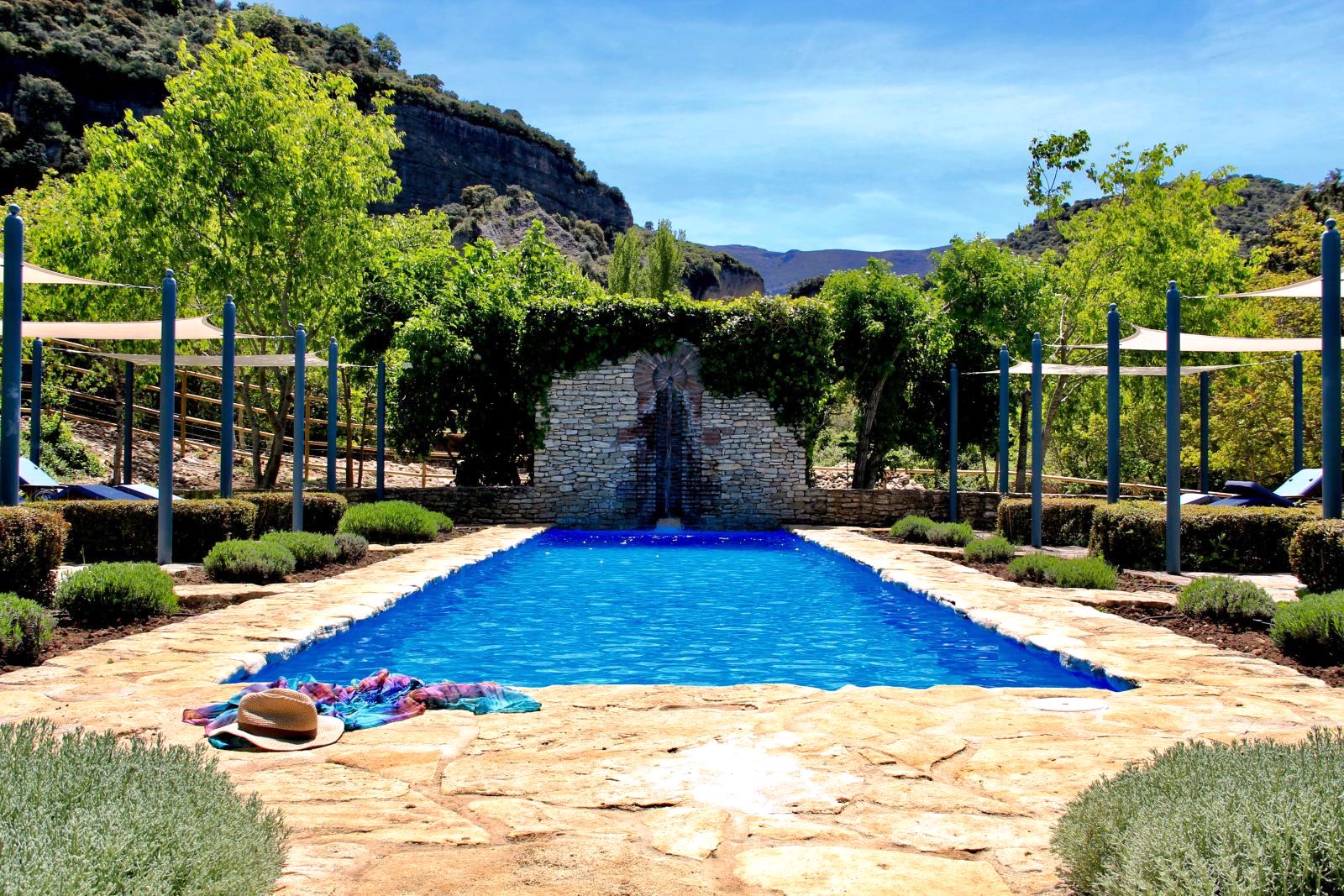 swimming pool with fountain in a stone wall with hills behind at villa Casa de Valle in Andalucia, Spain