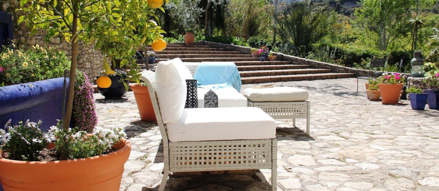 sun terrace with white wicker furniture and large terracotta plant pot with orange tree at villa Casa de Valle in Andalucia, Spain