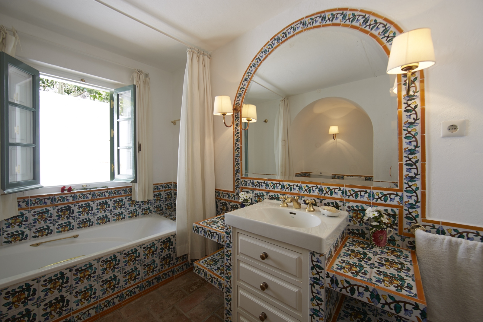 Bathroom with patterned tiles, bath, sink, large mirror, lights and window at Torre de Tramores in Andalucía, Spain