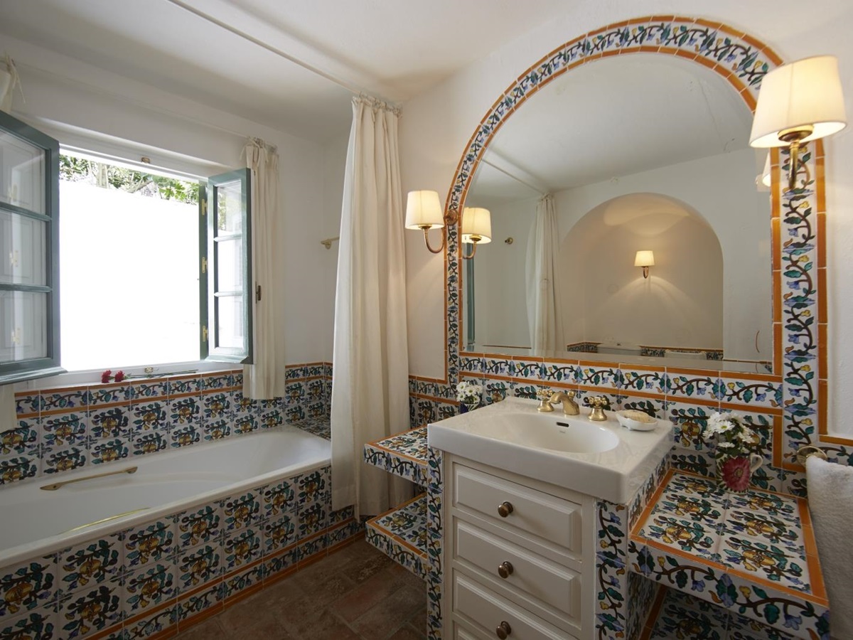 Bathroom with patterned tiles, bath, sink, large mirror, lights and window at Torre de Tramores in Andalucía, Spain
