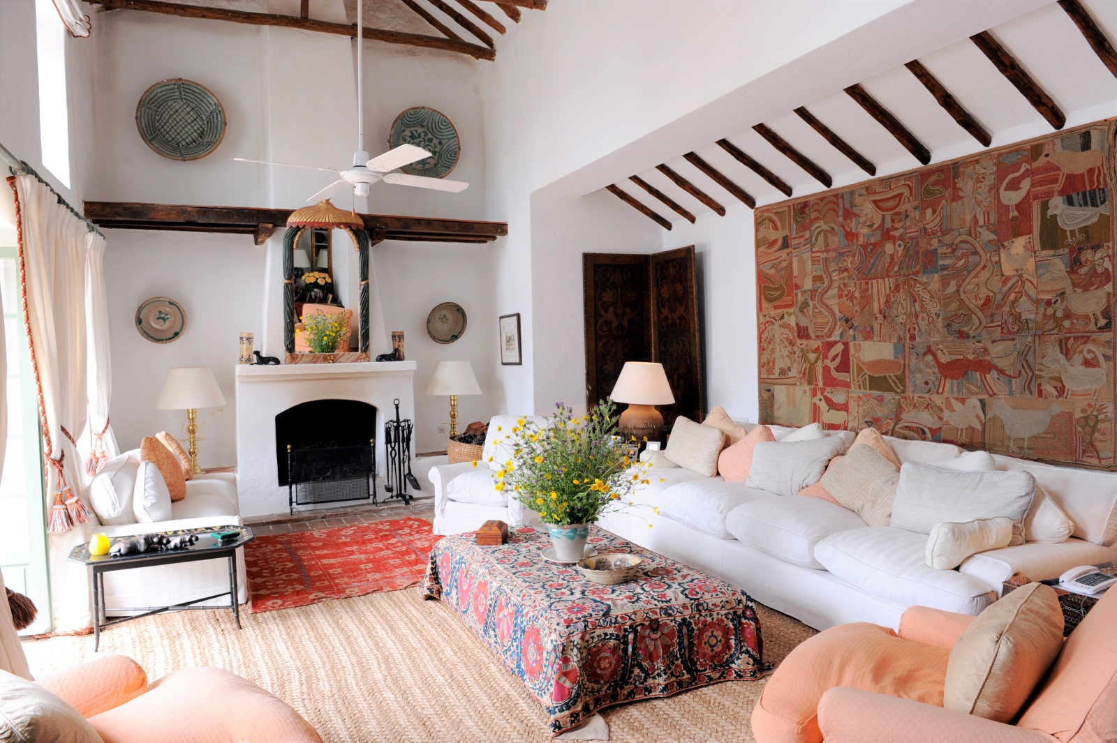 Living room with sofas, armchairs, coffee table, flowers, tapestry and fireplace at Torre de Tramores in Andalucía, Spain