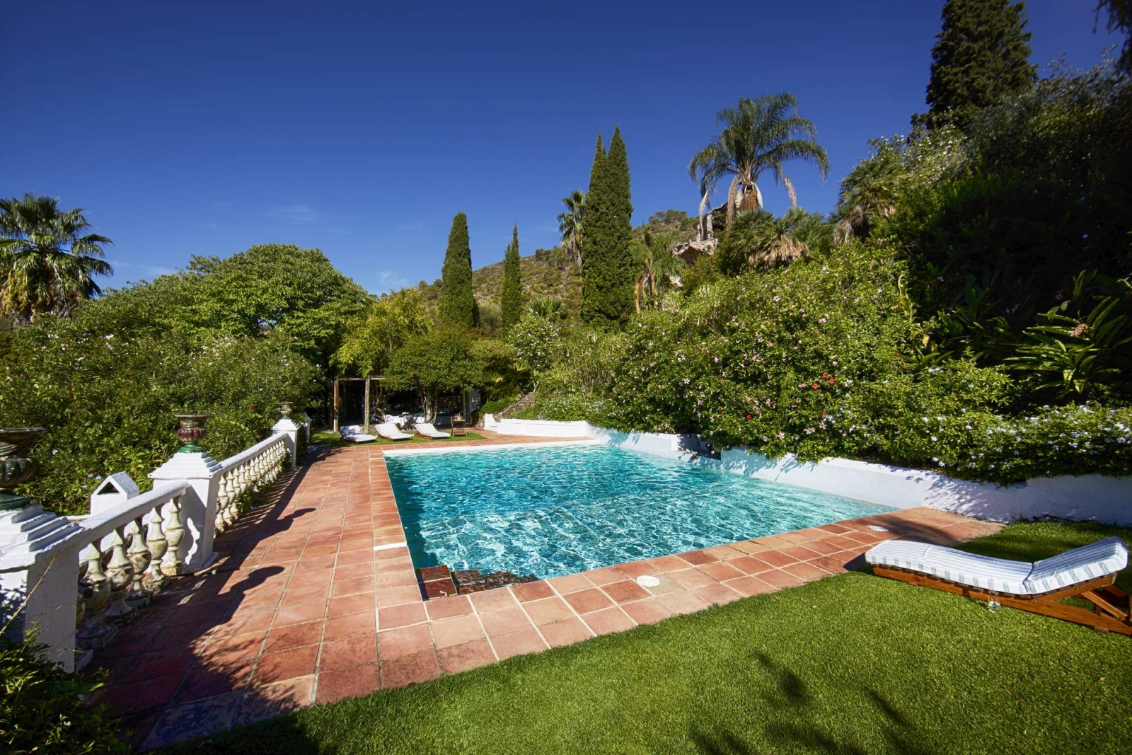 Pool and pool area with sun loungers, grass, terracotta tiles and plants at Torre de Tramores in Andalucía, Spain