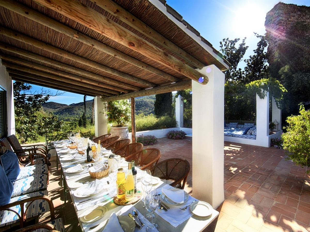 Covered outdoor dining area on terrace with long table, chairs and mountain view at Torre de Tramores in Andalucía, Spain
