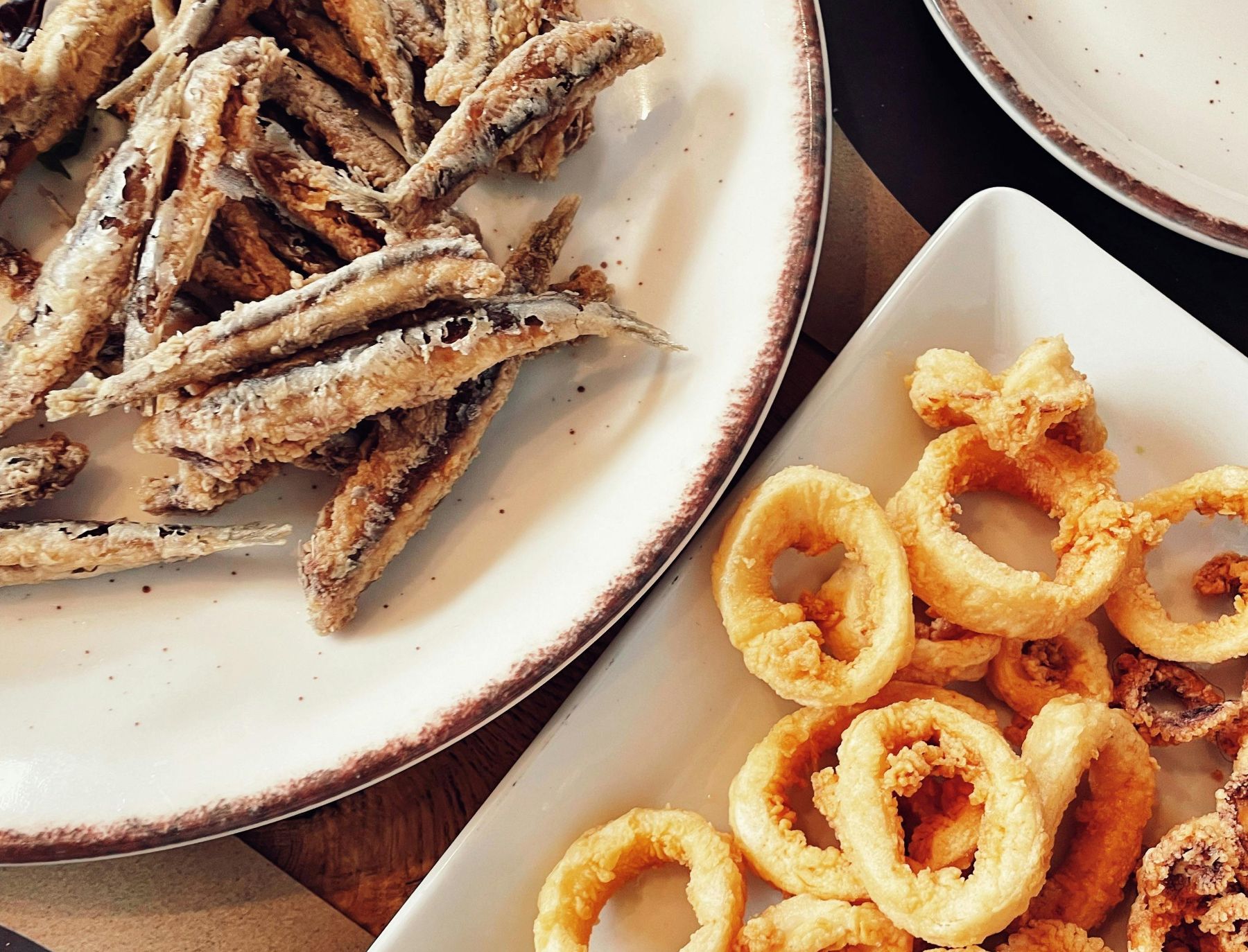 Plates of lightly fried anchovies and calamari rings in batter