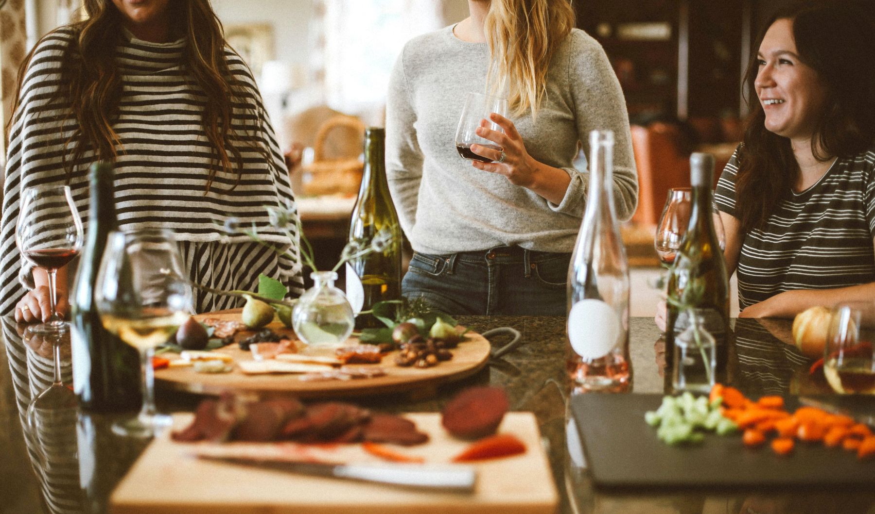 Three friends preparing meal and drinking wine in a kitchen