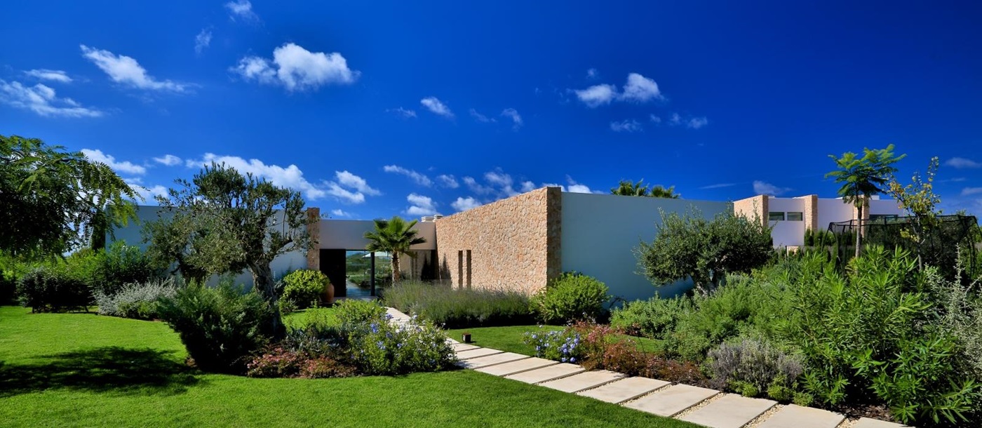 Front garden with green grass, trees, flowers and plants at Cala Comte in Ibiza, Spain