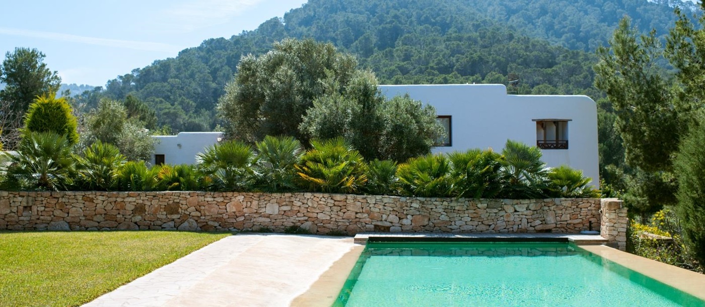 Pool area with grass and view of villa and surrounding hills at Casa Sabena on Ibiza, Spain