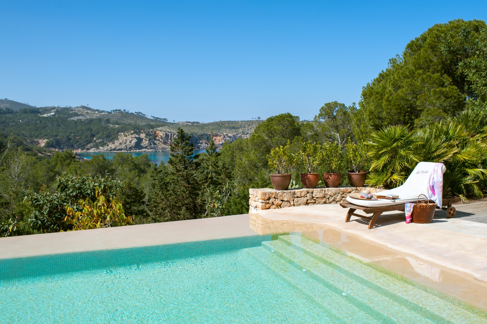 Pool area with patio, sun lounger, plants, trees and sea view at Casa Sabena on Ibiza, Spain