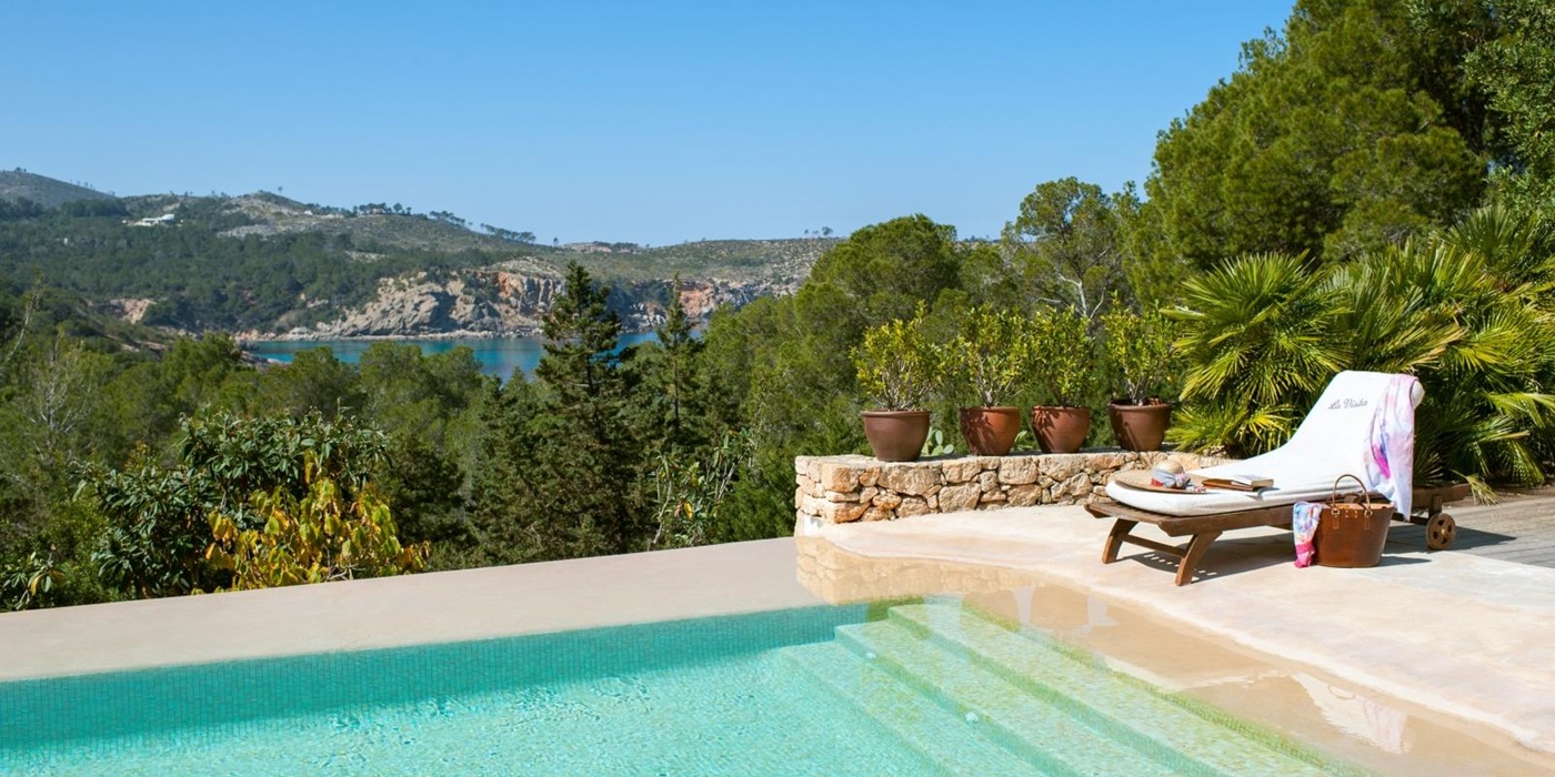 Pool area with patio, sun lounger, plants, trees and sea view at Casa Sabena on Ibiza, Spain