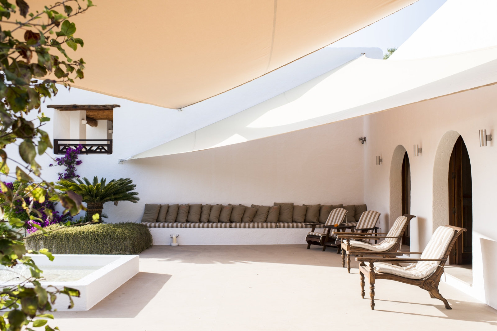 Covered outdoor lounge area with armchairs, sofa, fountain and flowers at Casa Sabena on Ibiza, Spain