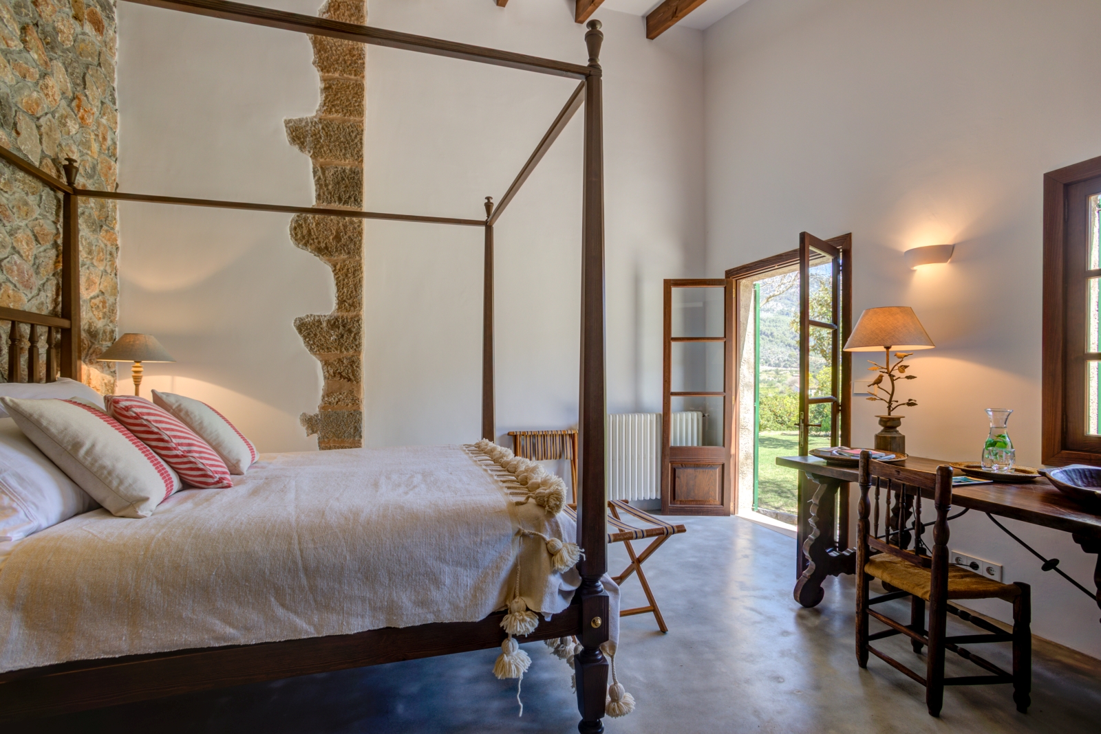 Double bedroom in annex with four-poster double bed, desk, chair, lamp and French doors at Can Canals in Mallorca, Spain