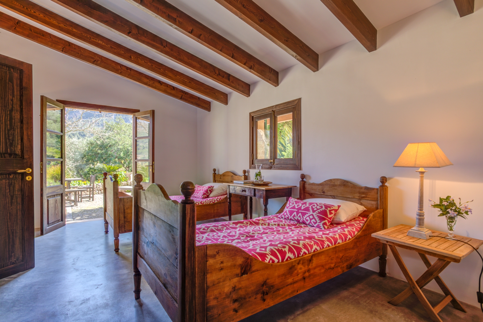Twin bedroom in annex with two bedside tables, lamp, small window and French doors to garden at Can Canals in Mallorca, Spain