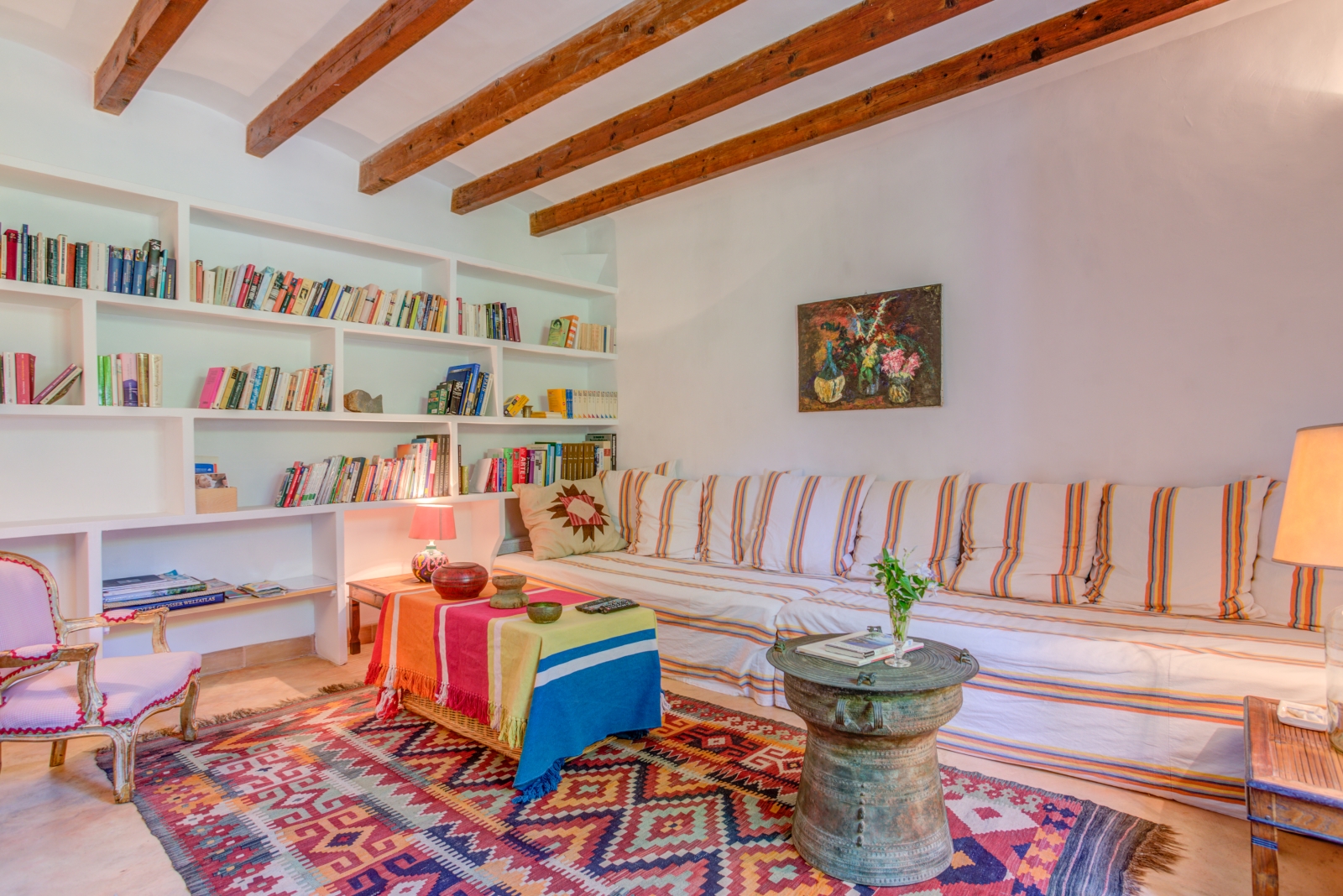 Library room with extra-large sofa, armchair, four coffee tables, books, painting and rug at Can Canals in Mallorca, Spain
