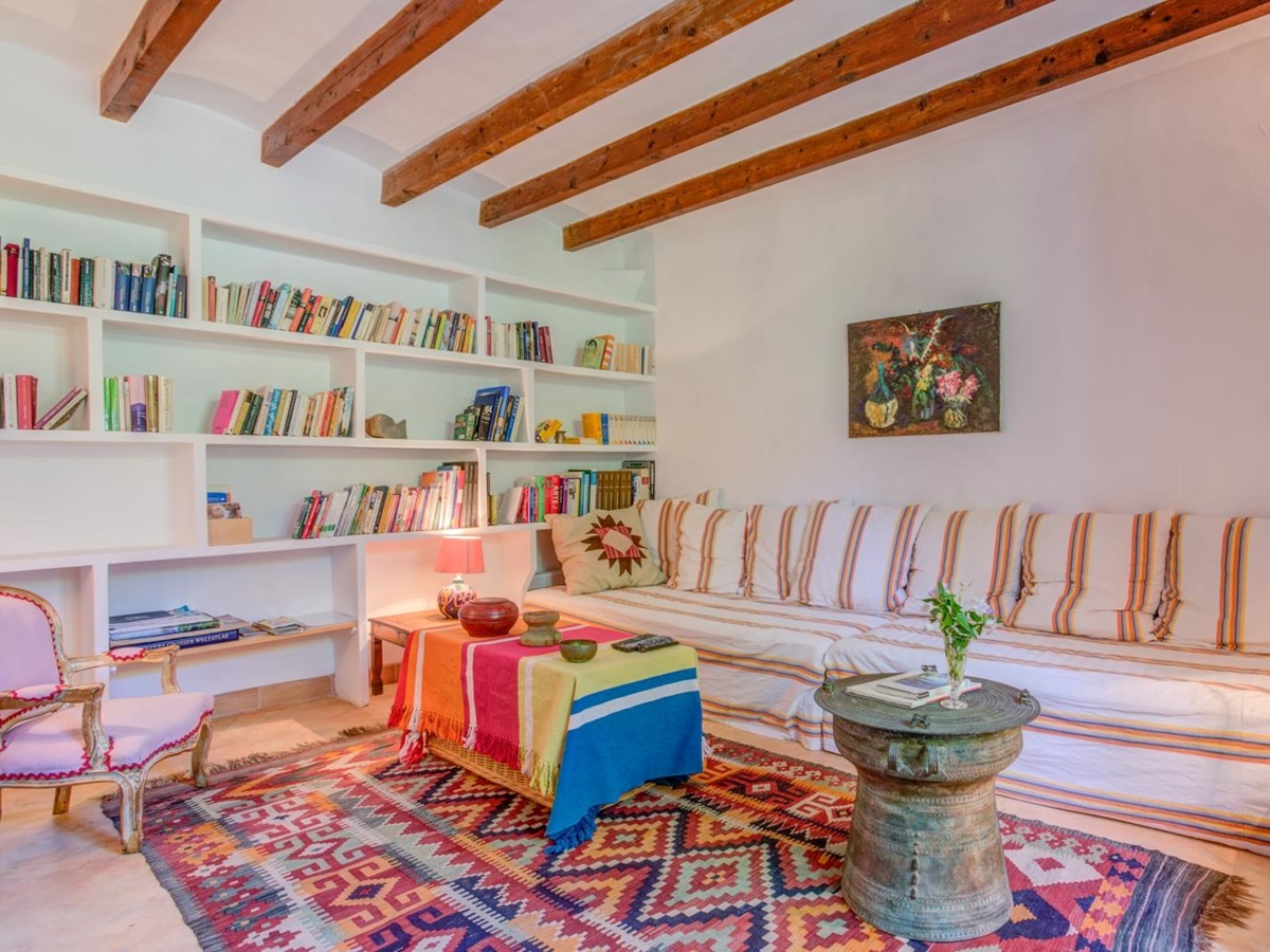 Library room with extra-large sofa, armchair, four coffee tables, books, painting and rug at Can Canals in Mallorca, Spain