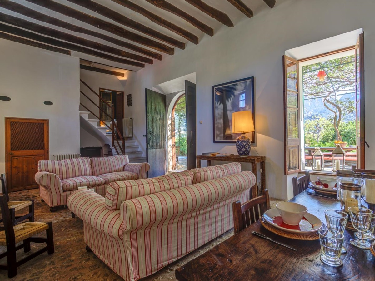 Lounge with dining table, chairs, crockery, two sofas, staircase, window and French doors at Can Canals in Mallorca, Spain