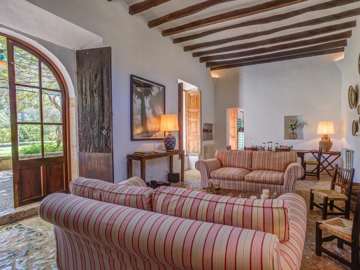 Lounge with sofas, chairs, fireplace, lamps, console table, large window and French doors at Can Canals in Mallorca, Spain