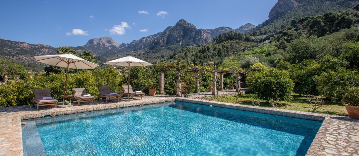 Pool with four sun loungers, two umbrellas, arbour with stone pillars and view of mountains at Can Canals in Mallorca, Spain