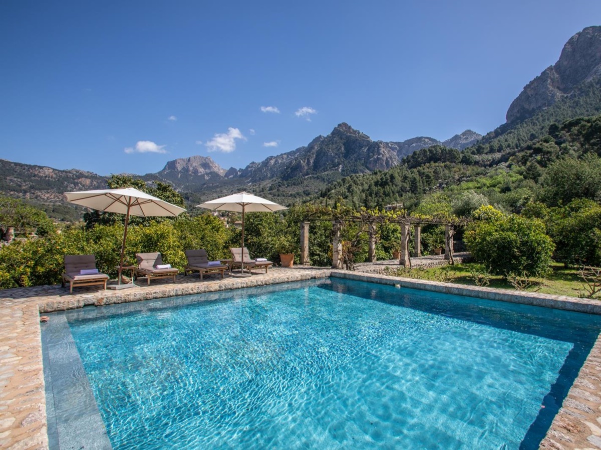 Pool with four sun loungers, two umbrellas, arbour with stone pillars and view of mountains at Can Canals in Mallorca, Spain