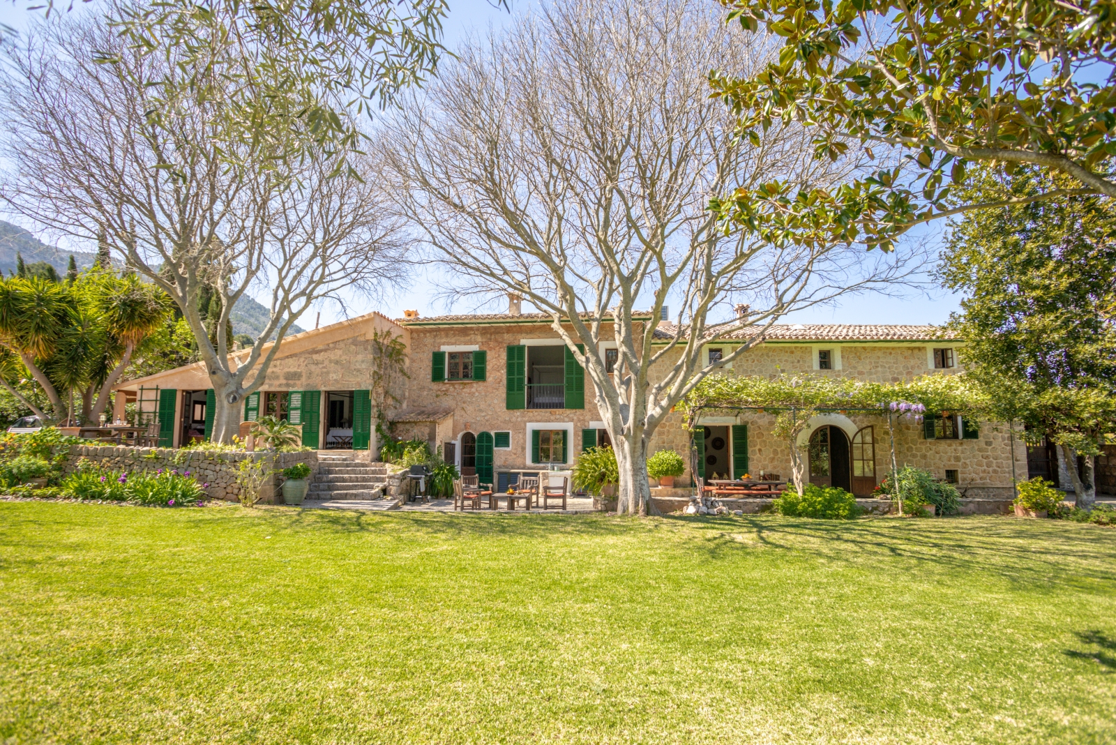 Outdoor view of villa with trees, grass, flowers, arbour and garden furniture at Can Canals in Mallorca, Spain