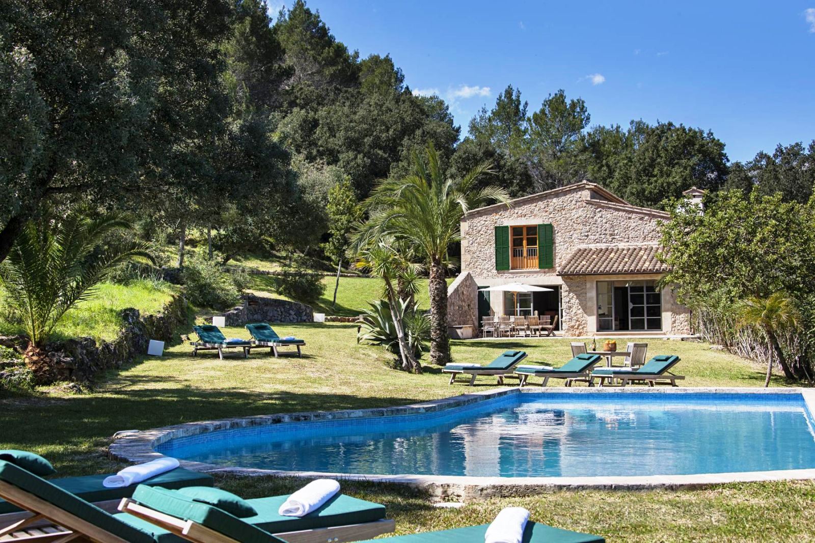 swimming pool with sunbeds with green cushions in garden with villa can jardine verde in Mallorca in the background