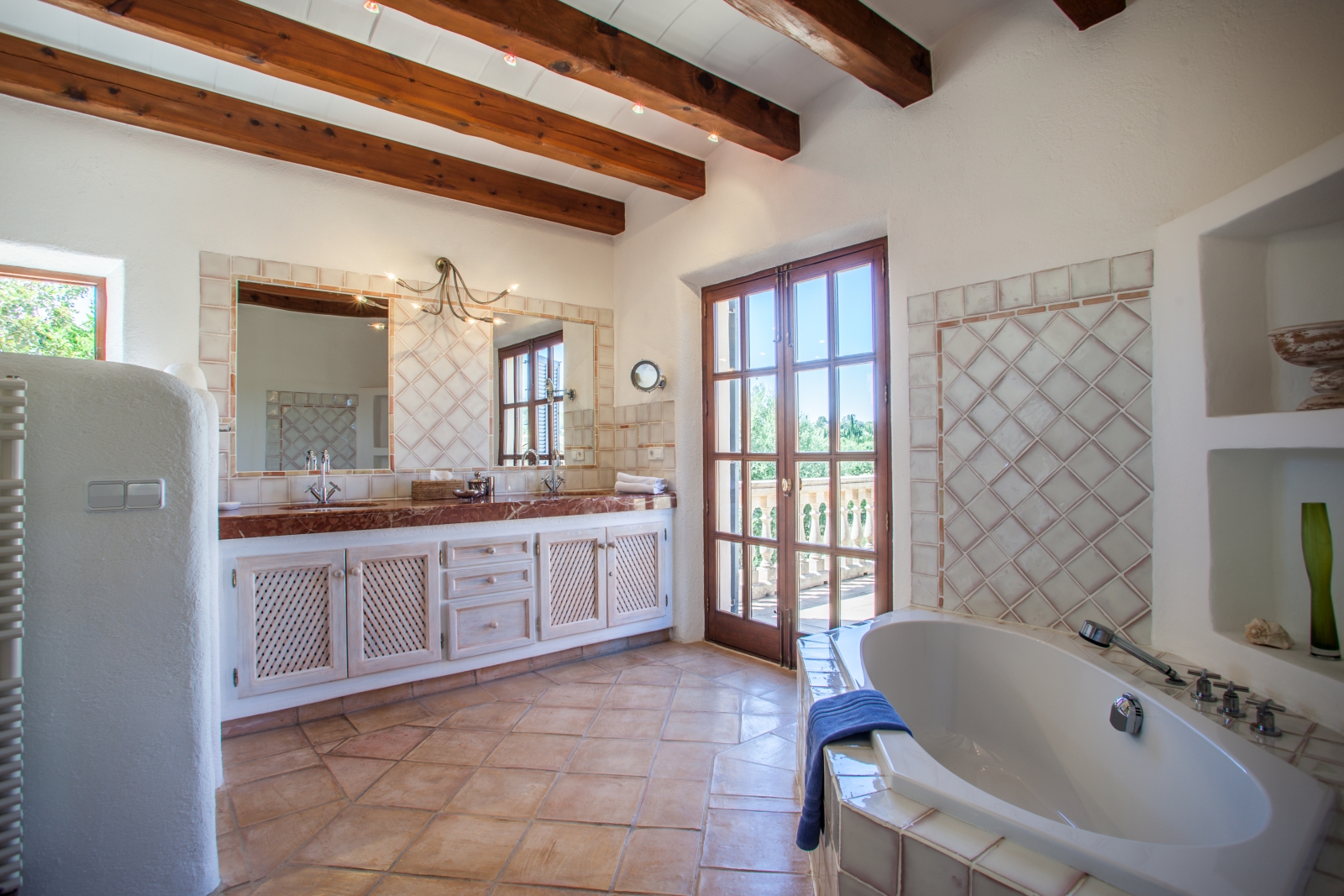 Bathroom with bath, two sinks, two mirrors, ceiling beams and French doors at Can Suelo in Mallorca, Spain