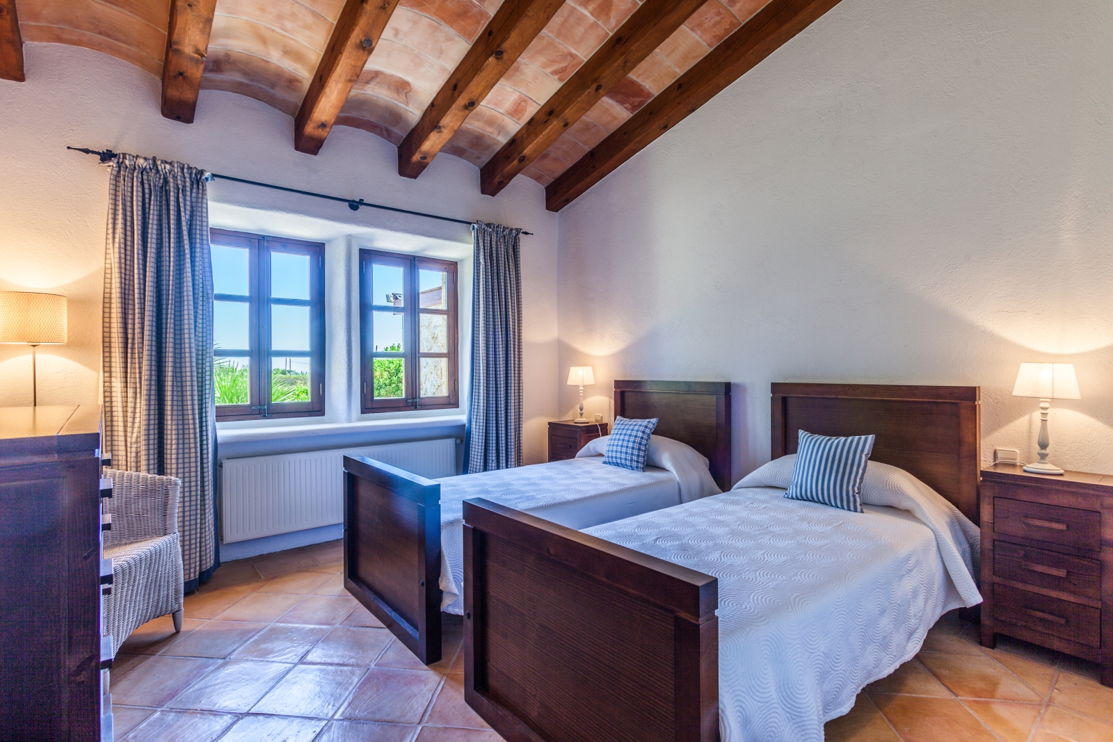 Bedroom with twin beds, bedside tables, lamps, armchair, chest of drawers and windows at Can Suelo in Mallorca, Spain