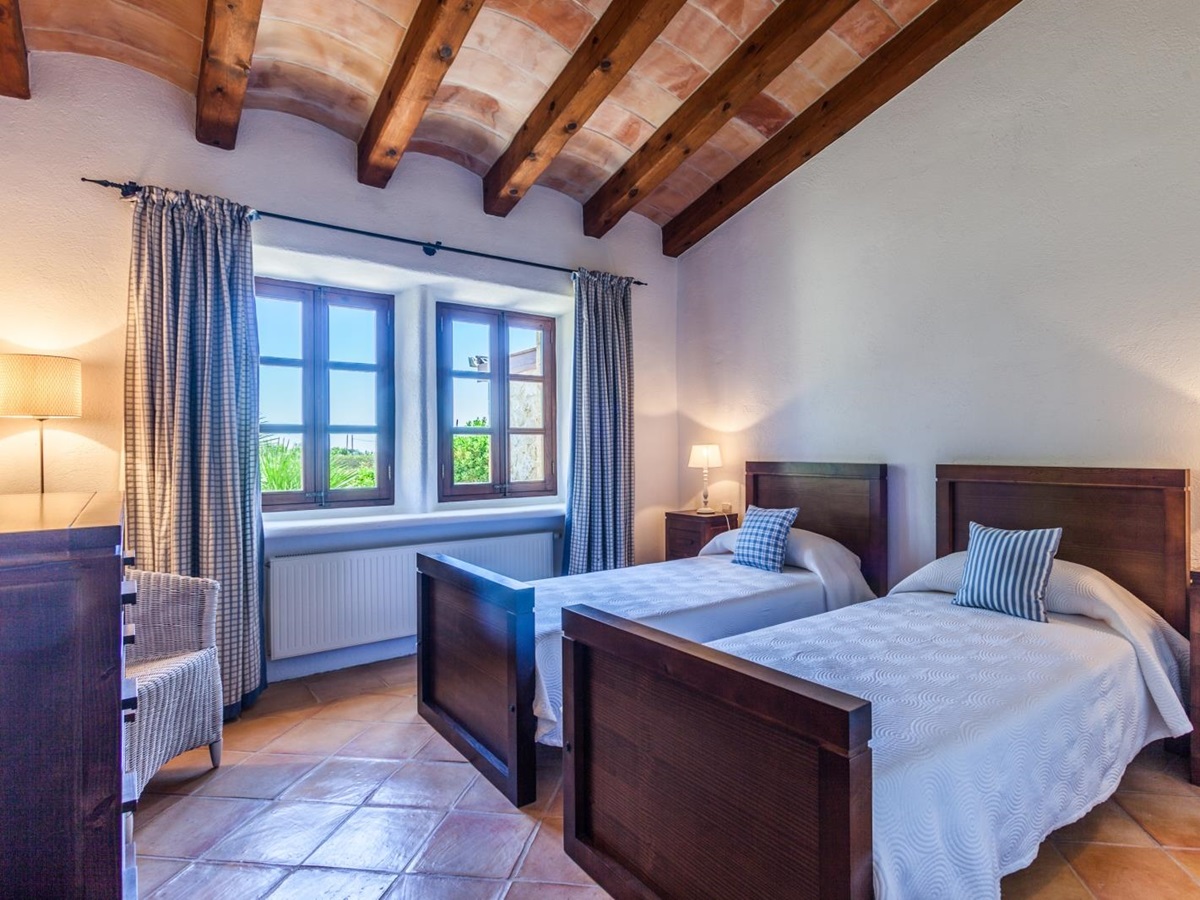 Bedroom with twin beds, bedside tables, lamps, armchair, chest of drawers and windows at Can Suelo in Mallorca, Spain