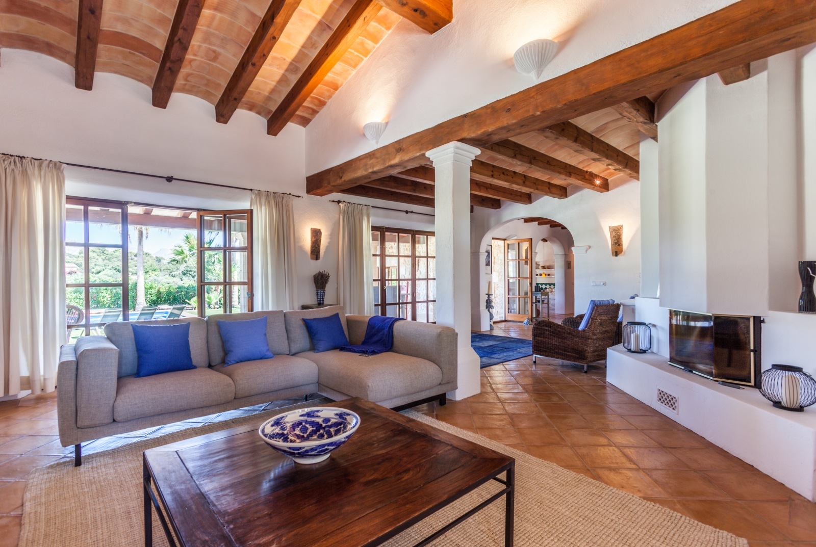 Lounge with sofa, blue cushions, wooden coffee table, fireplace, armchairs and French doors at Can Suelo in Mallorca, Spain