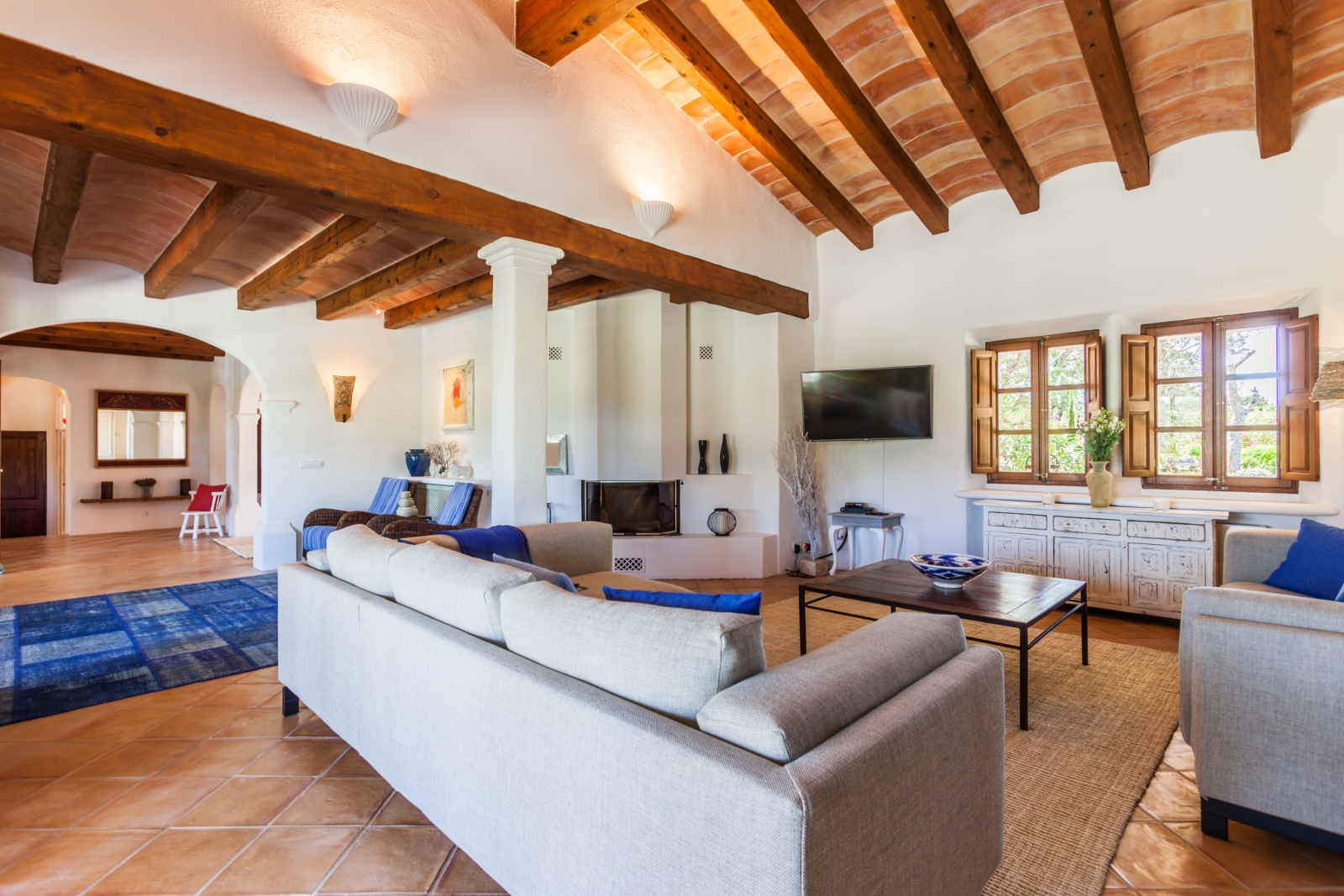 Lounge with two sofas, blue pillows, coffee table, cabinet, windows, TV, fire & blue rug at Can Suelo in Mallorca, Spain