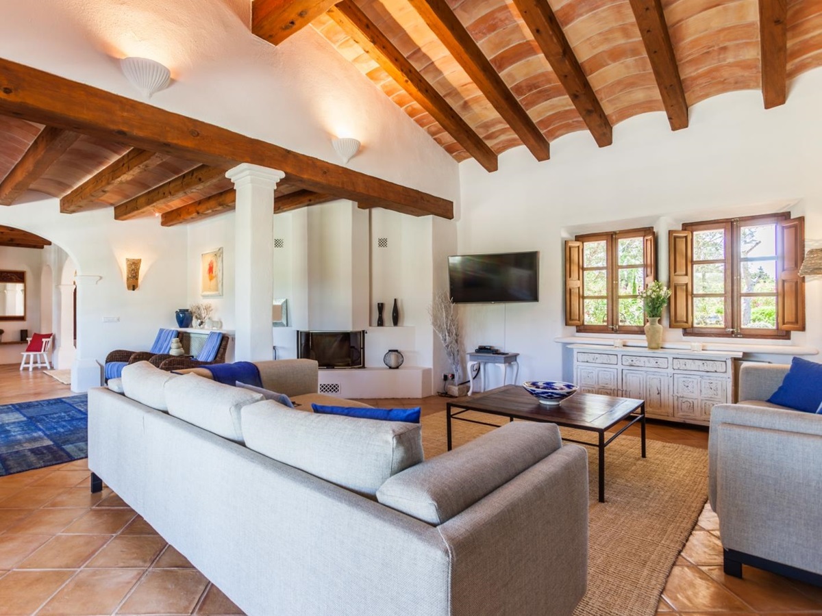 Lounge with two sofas, blue pillows, coffee table, cabinet, windows, TV, fire & blue rug at Can Suelo in Mallorca, Spain