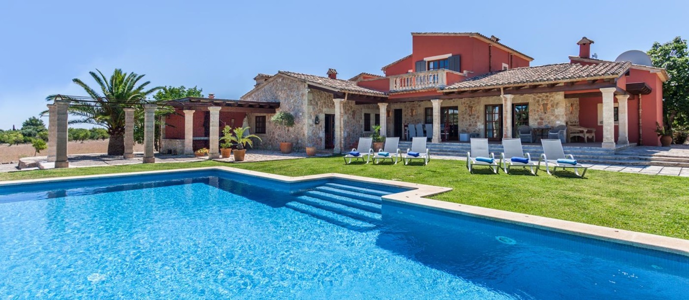 Pool with sun loungers and view of back of villa and garden at Can Suelo in Mallorca, Spain